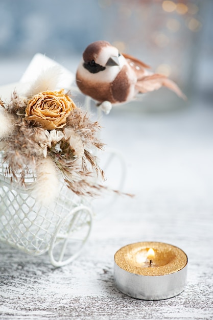 Bouquet of dry flowers on decorative bike with litle brown bird and lit candle on the table. Greeting card for wedding or holiday in natural tones