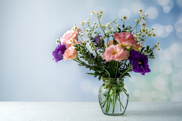 Bouquet of eustoma with boxwood and small-leaved branches on a table on a blue background