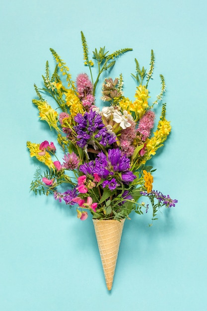 Bouquet field colored flowers in waffle ice cream cone on blue paper background