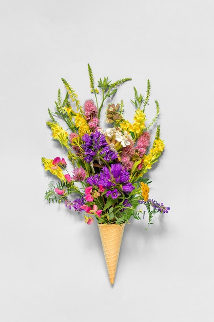 Bouquet field colored flowers in waffle ice cream cone on grey paper background Flat Lay Top view Mock up Concept Women's day or Mothers Day