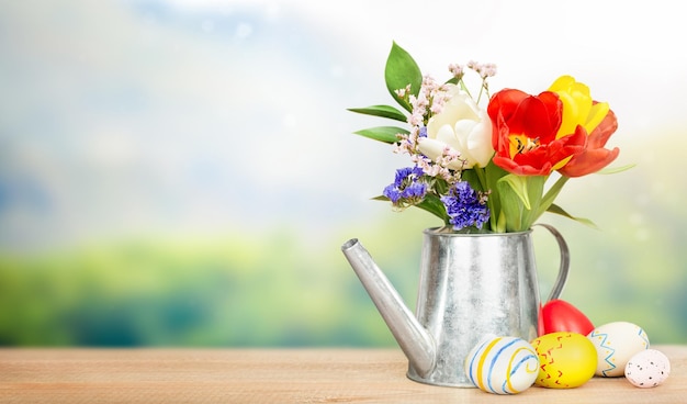 bouquet of flowers in a decorative watering can and Easter eggs on a wooden table