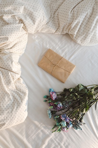 Bouquet of flowers and a gift covered in paper on crumpled white bed sheets