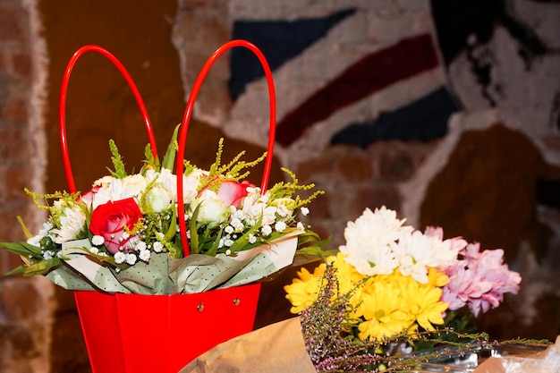 Bouquet of flowers in red basket and in craft paper against a blurred brick wall