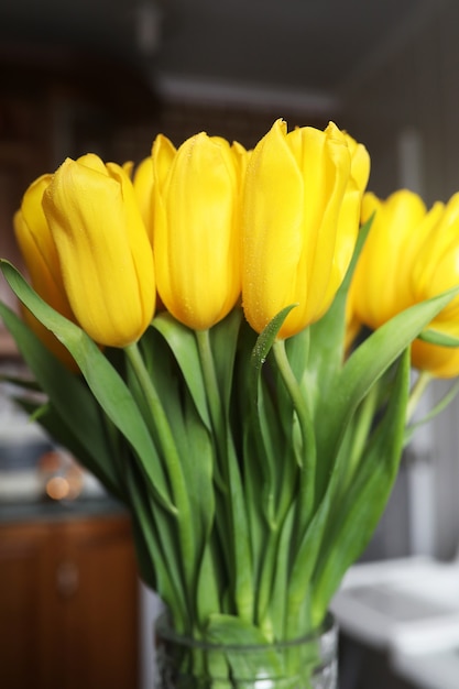 A bouquet of fresh yellow tulips in a vase on a table near the window