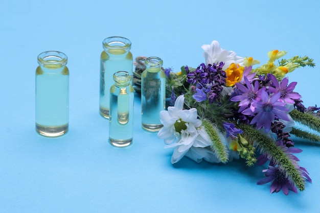 Bouquet from  wild flowers and bottles with essential oil on a  blue background