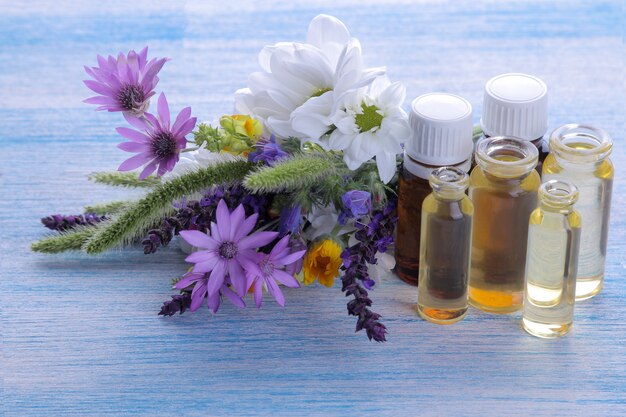 Bouquet from  wild flowers and bottles with essential oil on a  wooden blue table