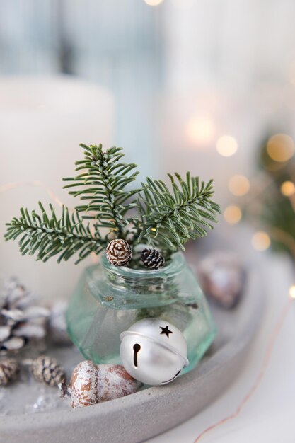 Bouquet of green spruce branches in vase white burning candles and silver christmas bells