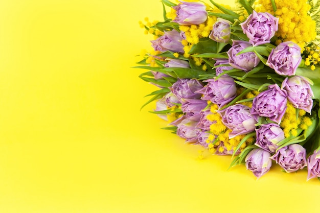 Bouquet of lilac tulips and yellow mimosas on yellow background, copy space, side view, closeup.