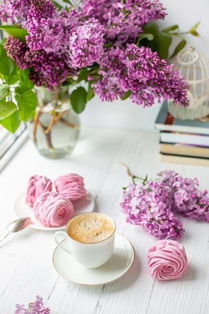 Bouquet of lilacs, cup of coffee, homemade marshmallow. Romantic spring morning.