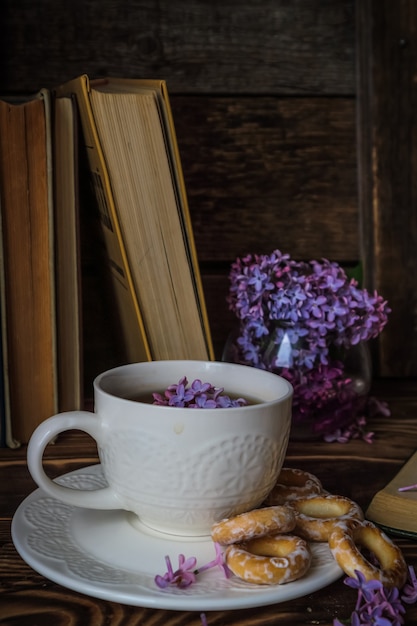 bouquet of lilacs and a white cup of tea on a wooden background