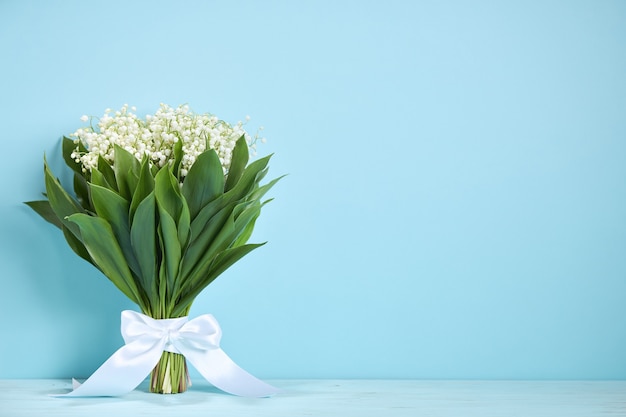 Bouquet of lilies of the valley with a white ribbon on a blue background