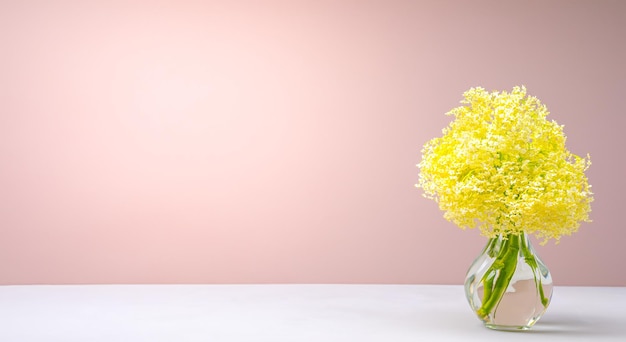 Bouquet of little yellow flowers in a glass vase on the table on a pink background