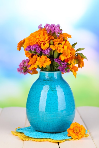 Bouquet of marigold flowers in vase on wooden table on natural background