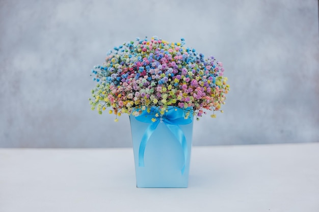 Bouquet of multicolored gypsophila in a blue box with a bow on a gray background