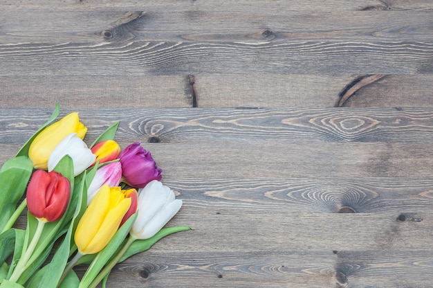 Bouquet of multicolored tulips in a corner on a background of wood.