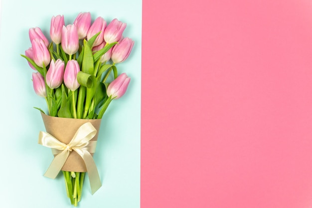 A bouquet of pale pink tulips tied with a ribbon and craft paper on a blue background