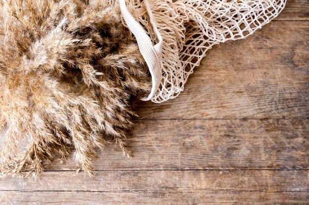 A bouquet of pampas grasses lies in a string bag on a wooden table