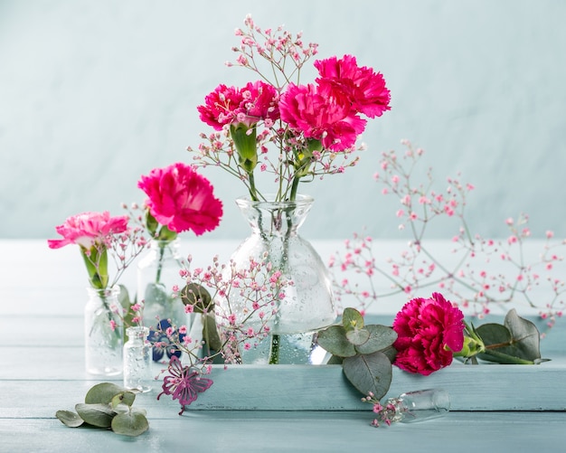 Bouquet of pink carnation in glass vase on light turquoise wooden surface. Mothers day, birthday greeting card. Copy space