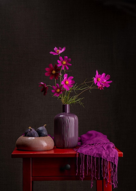 Bouquet of pink flowers in purple vase Nearby in earthenware are three blue ripe figs  