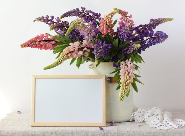 Bouquet of pink and purple peonies in a can and an empty rectangular frame on the table.