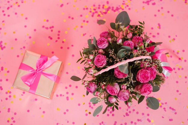 Bouquet of pink roses in a wicker basket and a gift box with a bow