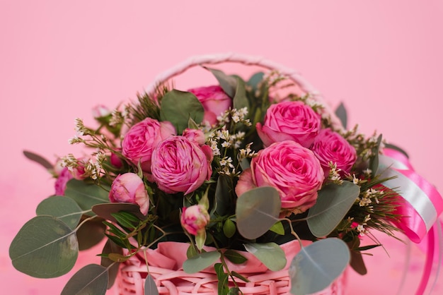 Bouquet of pink roses in a wicker basket on a pink table background Birthday Wedding Mother's Day Valentine's Day Women's Day Front view