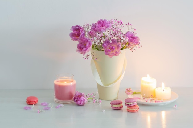 Bouquet of pink spring flowers and burning candles on  white table