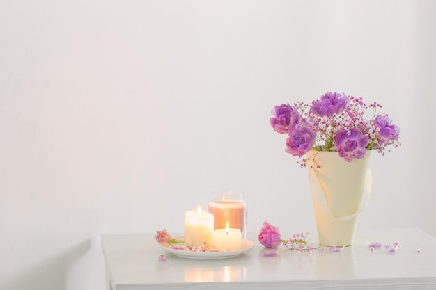 Bouquet of pink spring flowers and burning candles on  white table