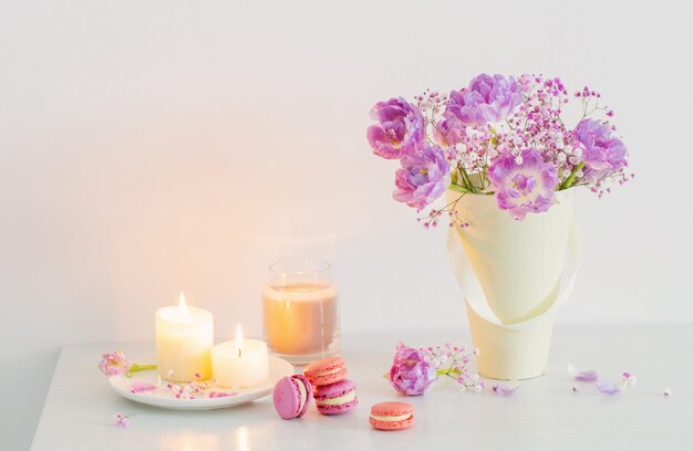 Bouquet of pink spring flowers and burning candles on white table