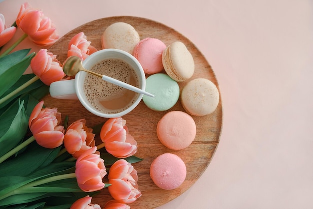 Bouquet of pink tulips cup of coffee and macaroons on pink background