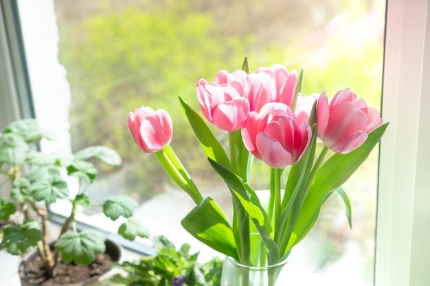 A bouquet of pink tulips in a transparent vase on the windowsill against the background of the window Bouquet of flowers as a gift to your beloved