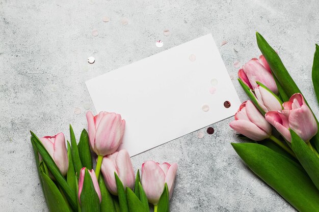 Bouquet of pink tulips with greeting card mock up on gray stone backround. flat lay with copyspace. greeting card concept.