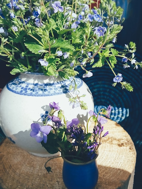 Bouquet of purple field flowers in white porcelain vase blue round wicker plate wooden background