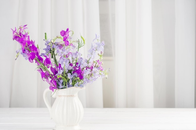 Bouquet of purple lupine flowers in a jag on white wooden table