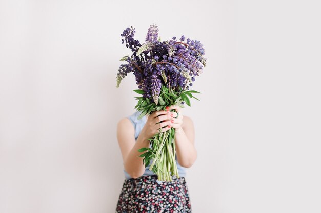 Bouquet of purple lupins in women hands on white surface Florist minimal concept Woman hold