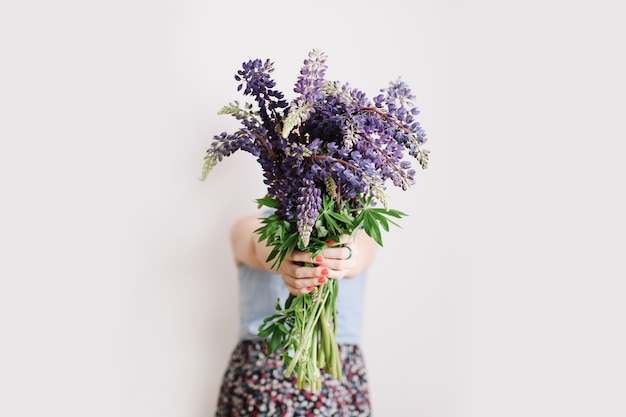 Bouquet of purple lupins in women hands on white surface Florist minimal concept