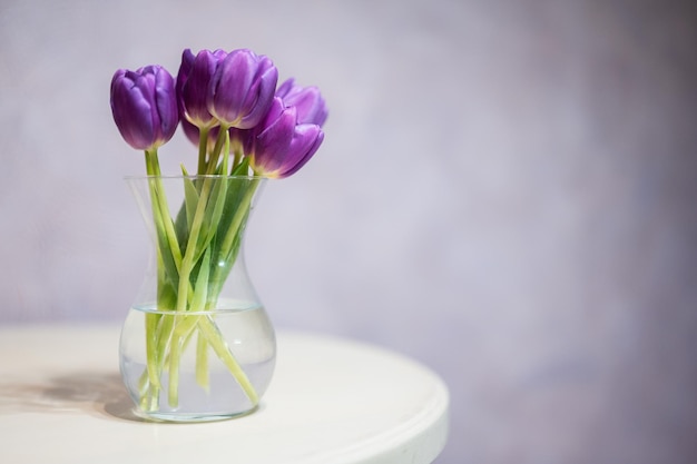 Bouquet of purple tulips with green leaves in glass vase