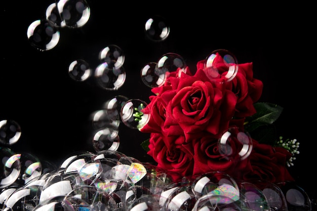 Bouquet of red roses, soap bubbles on black background, selective focus.