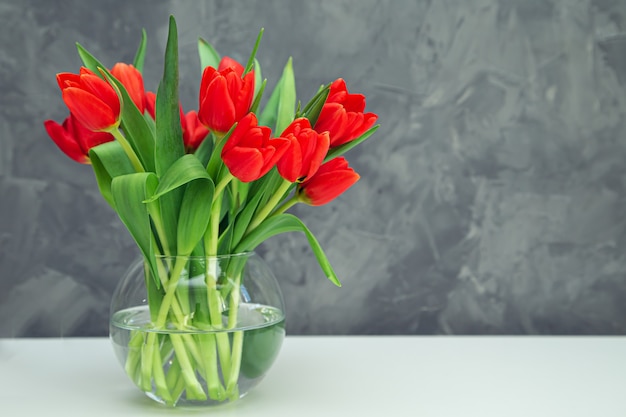 Bouquet of red tulips in a vase on a gray table. Spring festive mood.