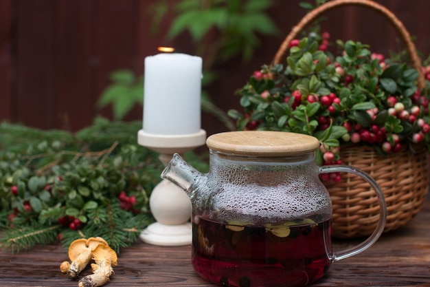 A bouquet of ripe red lingonberry berries in a wicker basket and a kettle of lingonberry tea Forest orange chanterelle mushrooms