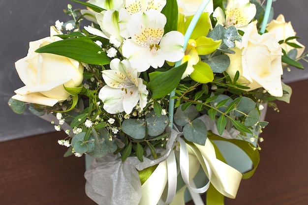 Bouquet of roses astralmeria and lilies in a basket of light green color on a gray background