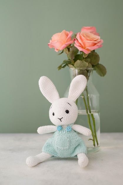 A bouquet of roses in a glass vase and a knitted white toy bunny  on a green background