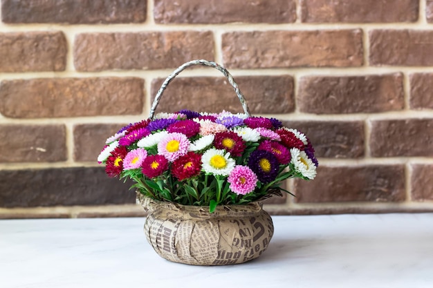 Bouquet of small chrysanthemums in the shape of a basket Bouquet on a white table against a brick wall