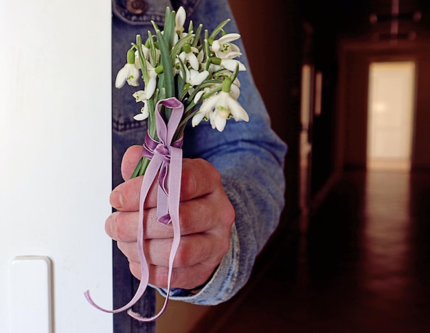 Bouquet of snowdrops in the hand of a man hiding behind a door closeup