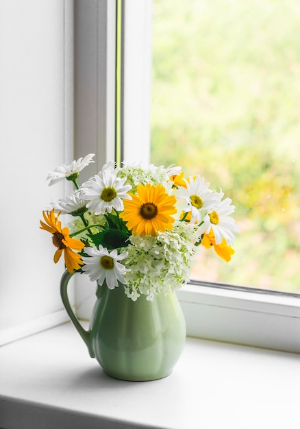 A bouquet of summer flowers of daisies hydrangeas in a vintage ceramic jug on the window in a bright room