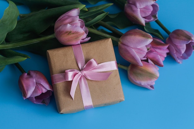 A bouquet of tulips and a gift box on a blue background