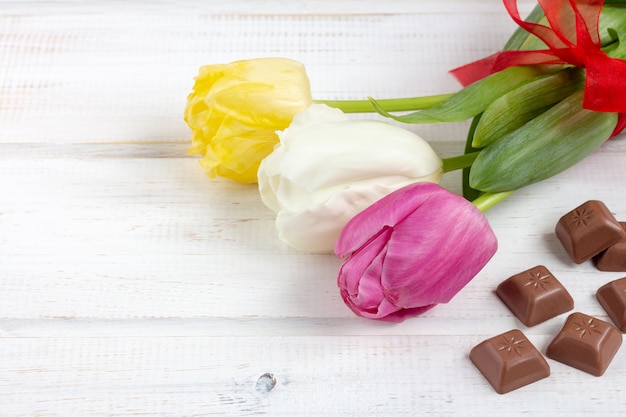 A bouquet of tulips (white, yellow, purple) with red ribbon and squares of chocolate