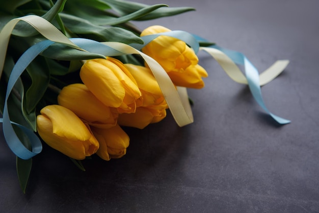 Bouquet of tulips with blue and yellow ribbon on a black background