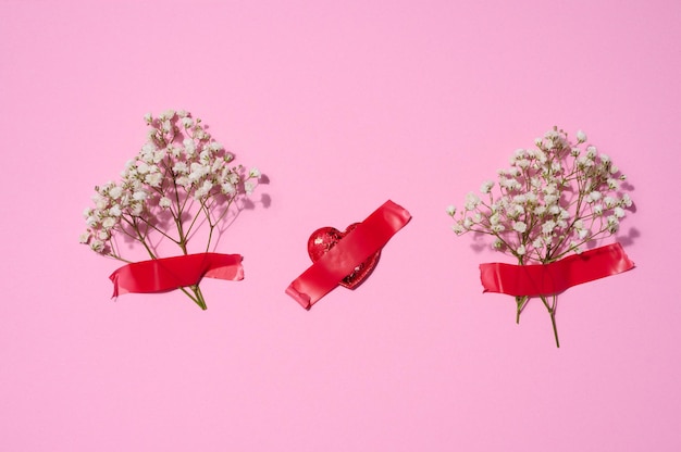 Bouquet of white gypsophila and red textile hearts on a pink background top view