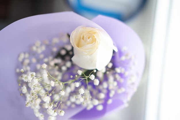 Bouquet of white roses in purple packaging on the windowsill top view